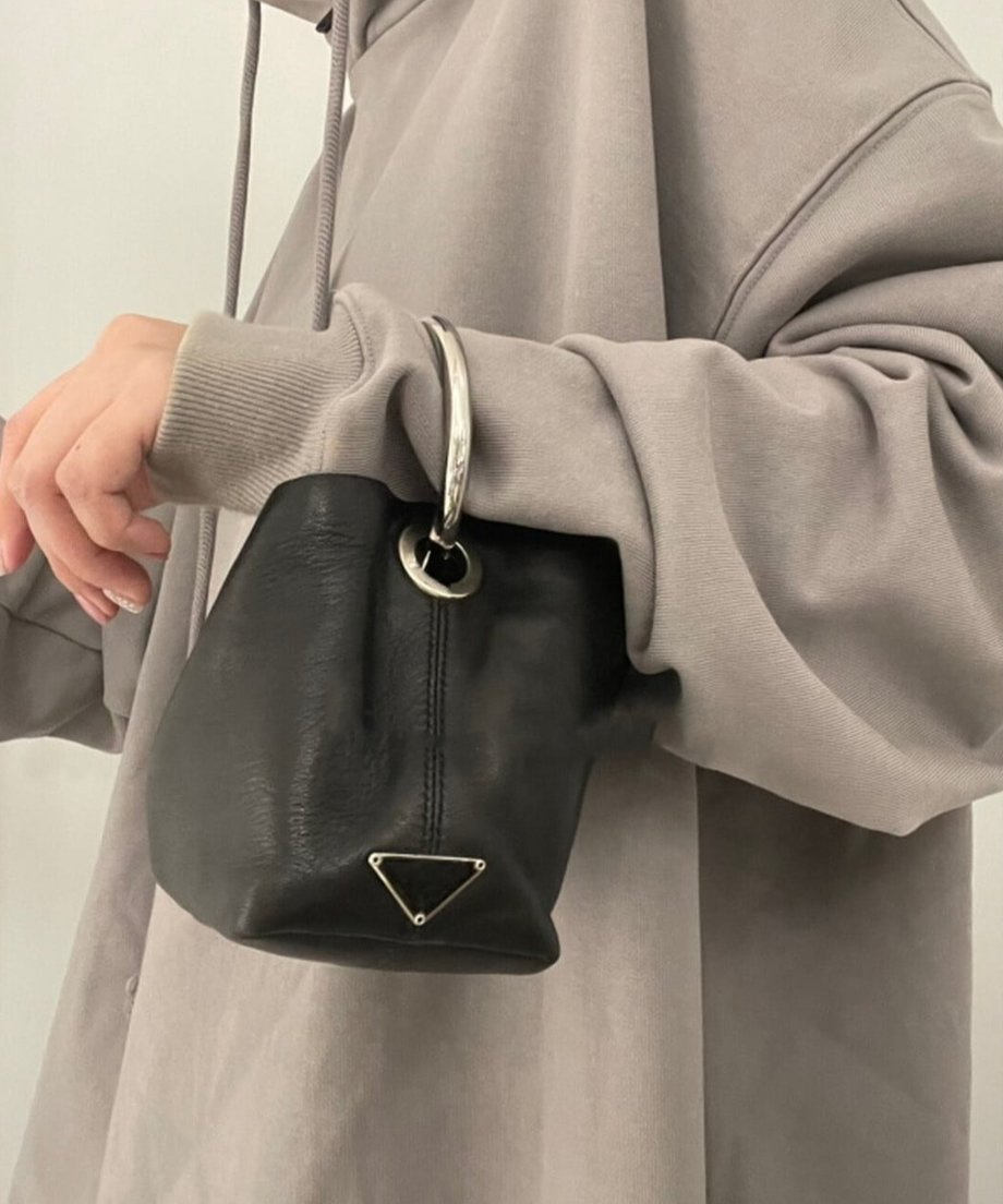 グレーのパーカーを着た女性が、シルバーのリングハンドルが付いた黒のPUレザーミニバッグを腕にかけている様子。