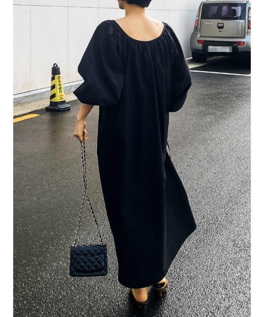 背面の広いラウンドネックとボリューム袖が特徴的な、黒のマキシ丈ワンピースを着用した女性の後ろ姿。