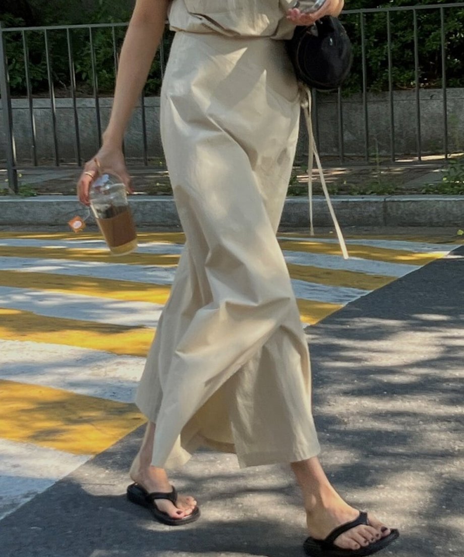 ベージュのラップスカートを着用して歩く姿。Aラインのシルエットと足元のトングサンダルが涼しげな印象。