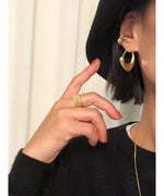 黒いニットを着用した女性の耳元で輝く、ゴールドの変形ニュアンスフープピアスとイヤーカフのスタイリング。