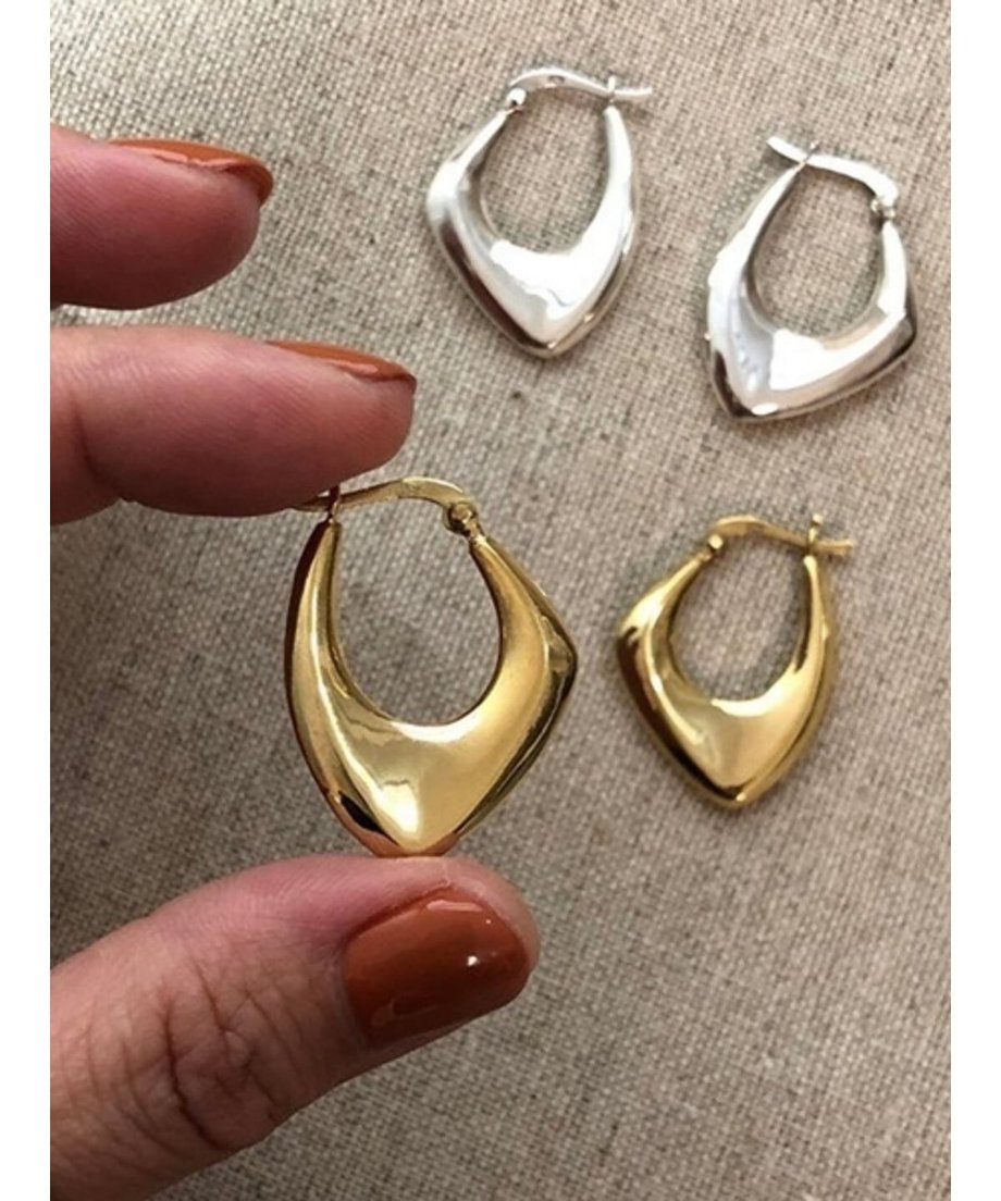 女性の指先に持たれたゴールドのフープピアス。光沢のある表面と独特なドロップ形状が特徴。