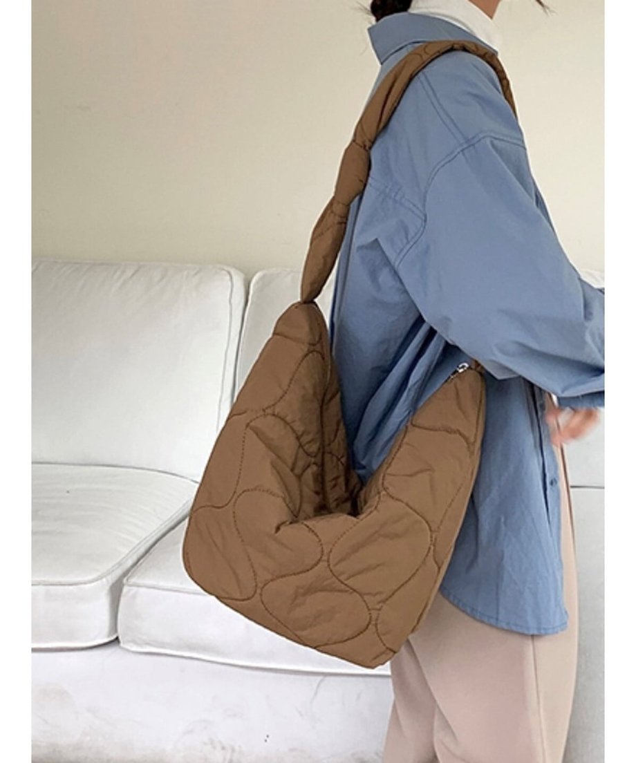 ブラウンのノット付きキルティングショルダーバッグを肩にかけ、横を向いて立っている女性。
