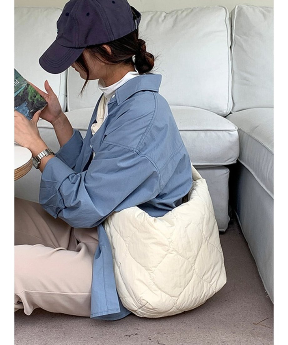 ホワイトのキルティングショルダーバッグを背中側へ回して肩掛けしている女性が床に座っているショット。