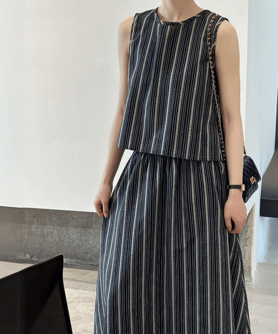 ネイビーのストライプ柄セットアップを着用し、黒のチェーンバッグを肩にかけた女性。