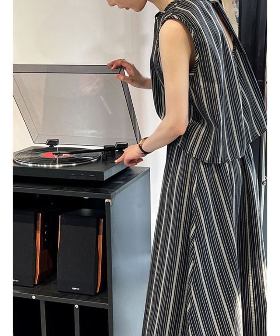 ネイビーのストライプセットアップを着用し、レコードプレーヤーに手を添える女性。