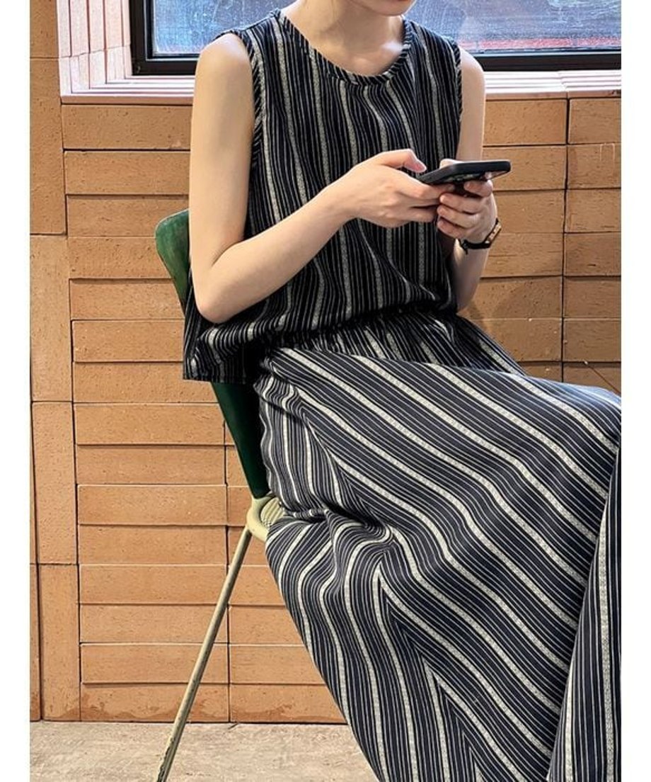 ストライプセットアップを着用し、椅子に座ってスマートフォンを操作する様子。