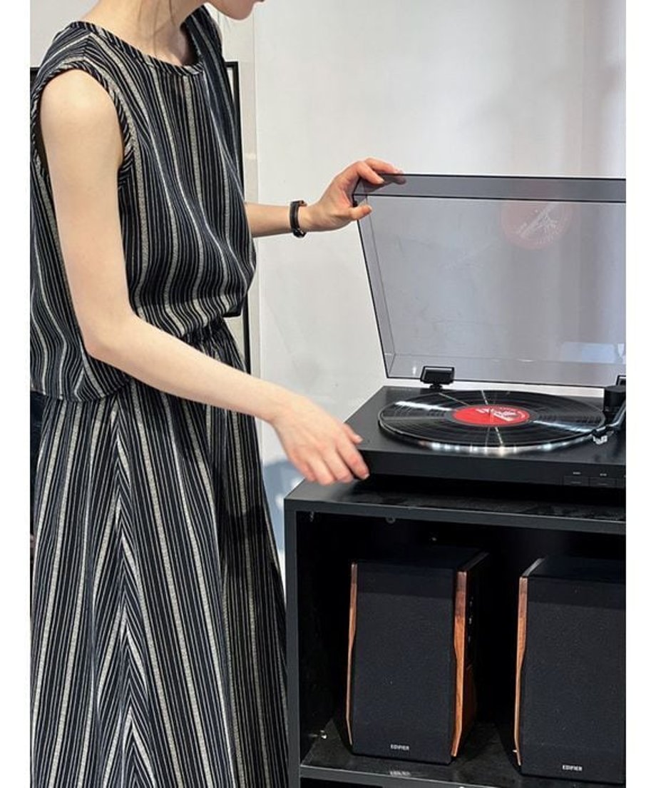ネイビーのストライプセットアップを着用し、レコードプレーヤーに手を添える女性。