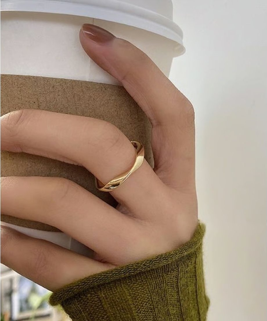 コーヒーカップを持つ女性の手元に着用された、ゴールドのツイストデザインリング