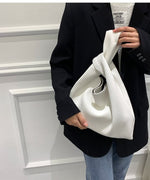 ホワイトのプリーツバッグを横向きに持ち、ディテールを見せたスタイリッシュなポージングの着用画像。