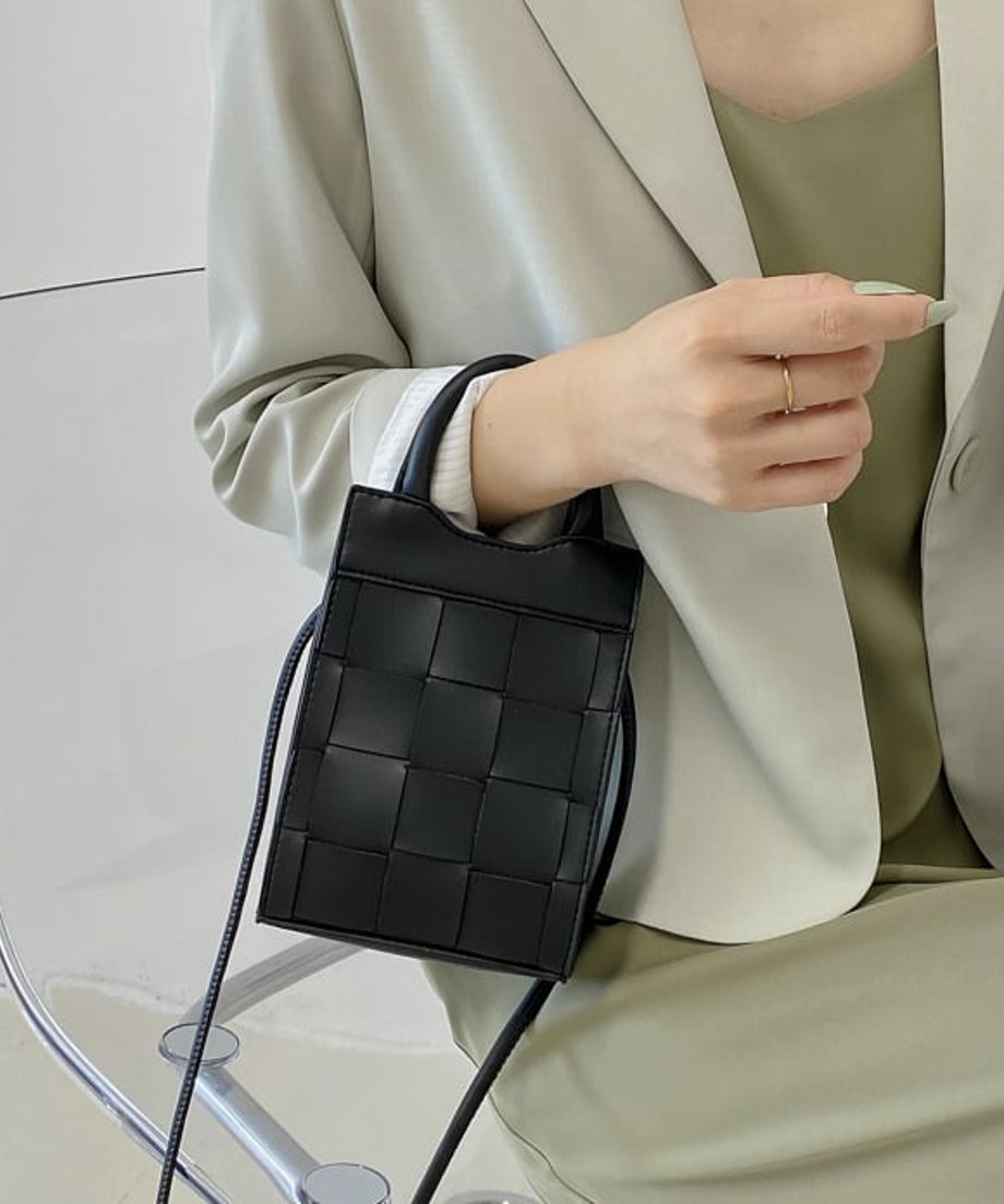 ブラックの2WAYバッグをハンドバッグとして持ち、手元に華奢なリングを添えたクローズアップ画像