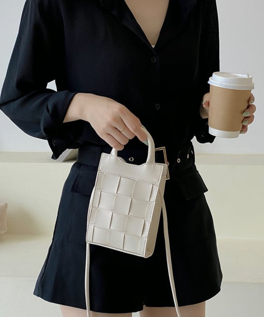 手にコーヒーを持ち、オフホワイトの2WAYミニバッグをハンドバッグとして持つ女性の姿