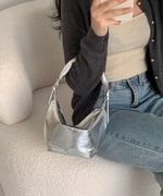 ソファに置かれたシルバーのメタリックバッグとデニムの組み合わせ。