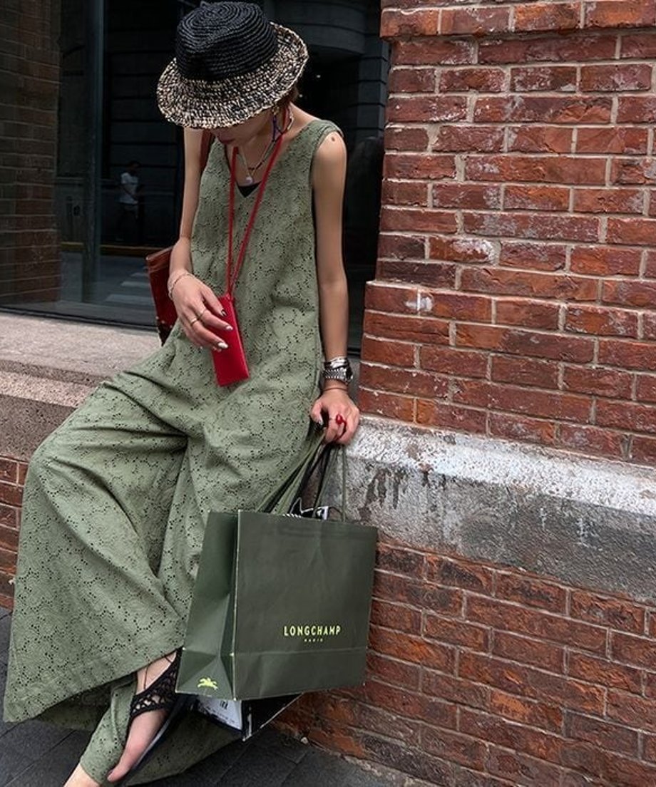 縁石に腰掛ける女性。ワイドパンツのボリューム感と、サンダルを合わせたリラックスした足元のスタイリング。