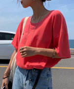 ピンクレッドのTシャツにシルバーのネックレスを重ね付けした、顔から下のアップ写真。
