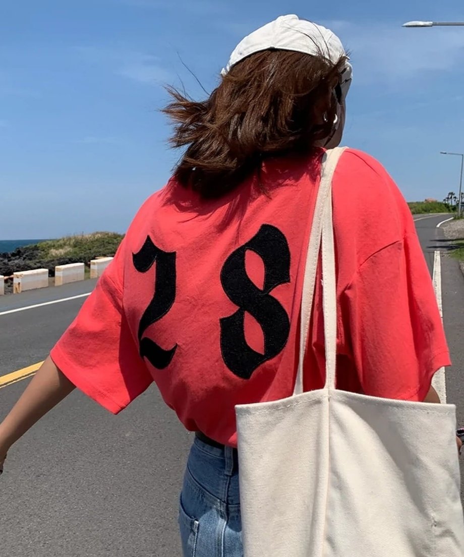 海辺の道路沿いで、背中のナンバリングが際立つTシャツを着用した女性の背後からのショット。