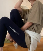 ブラウンベージュのTシャツと黒いレギンスを合わせ、腰に白いカーディガンを巻いたリラックスした座り姿。