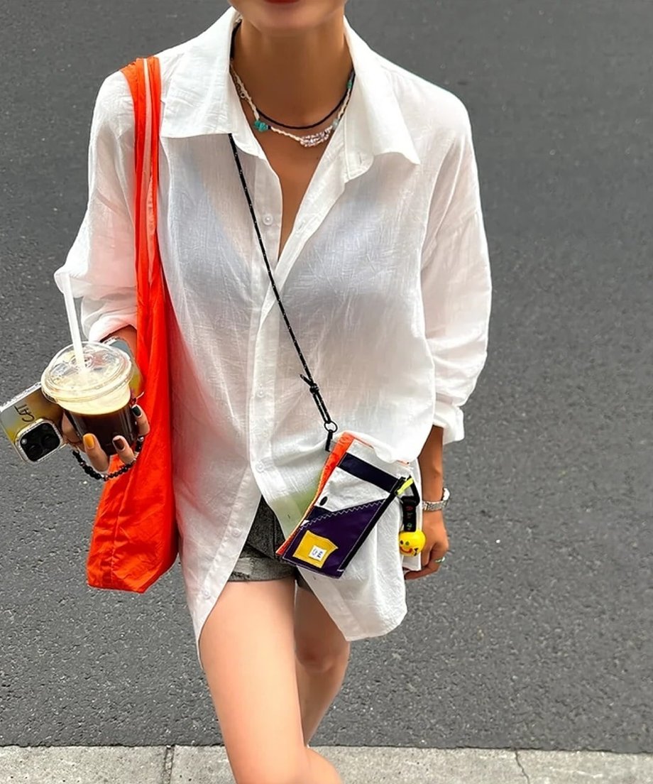 透け感のある白いシャツとデニムショートパンツを着用し、アイスコーヒーを持って歩く女性のクローズアップ。