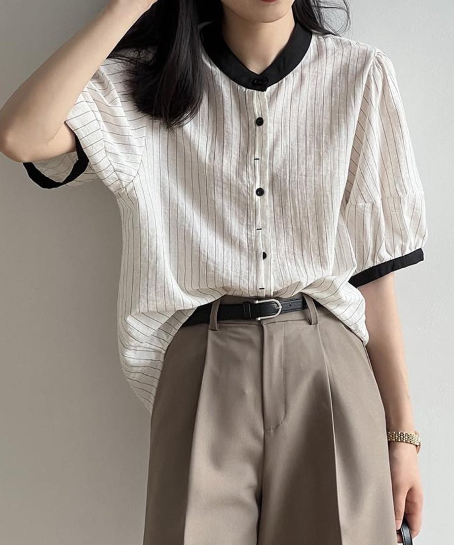 ストライプ柄シャツをベージュのタックパンツにハーフインし、黒のベルトでウエストマークしたコーディネート。