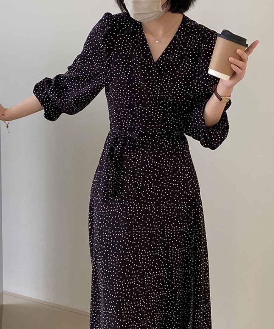 Vネックのドット柄ワンピースを着用し、手にコーヒーカップを持つ女性の正面アップ。
