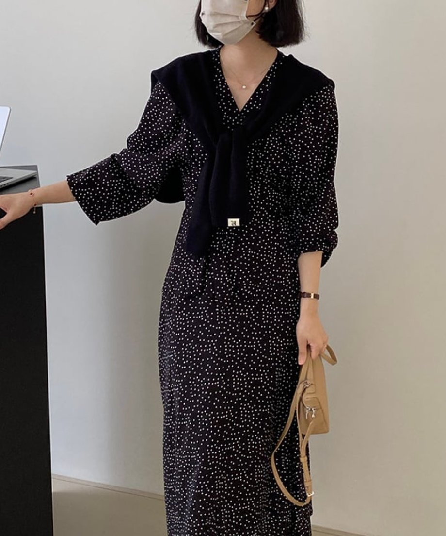 細かなドット柄のVネックロングワンピースに黒のカーディガンを肩掛けした女性のコーディネート。
