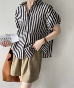 手に雑誌を持ち、ストライプブラウスのゆったりとしたサイズ感とシルエットを強調した全身カット。