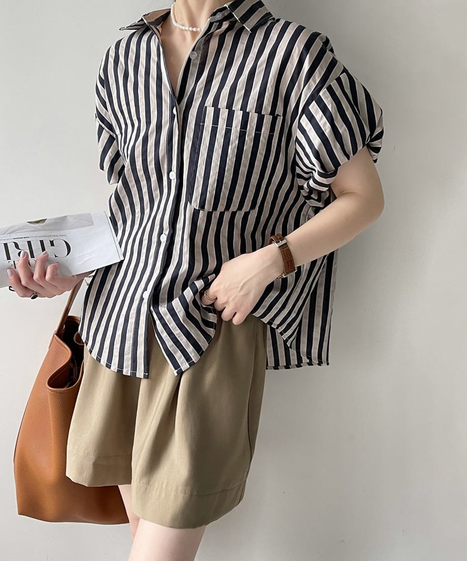 手に雑誌を持ち、ストライプブラウスのゆったりとしたサイズ感とシルエットを強調した全身カット。