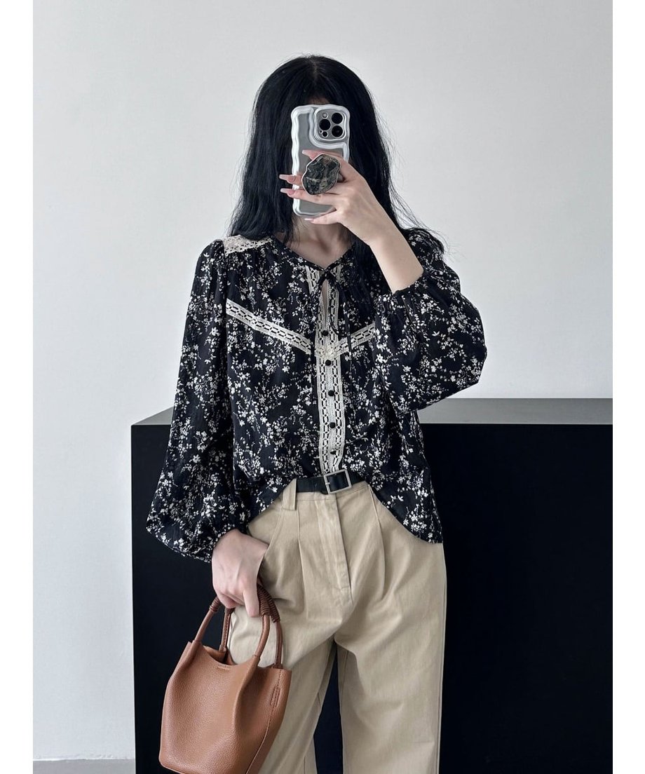 ブラックの小花柄ブラウスとベージュのチノパンを組み合わせた女性が自撮りしている画像。