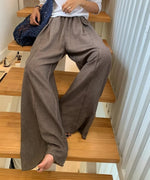 リネン混ワイドパンツを履いて階段に座る女性。動きのあるシルエットと素材の光沢感。
