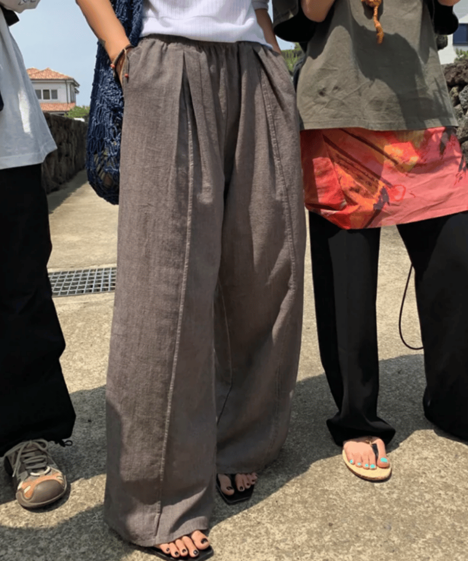 屋外で並ぶ友人たちの足元。中央の人物がライトブラウンのタック入りワイドパンツを着用。