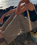 岩場に座る女性。ゆったりとしたワイドパンツのボリューム感と海辺のロケーション。
