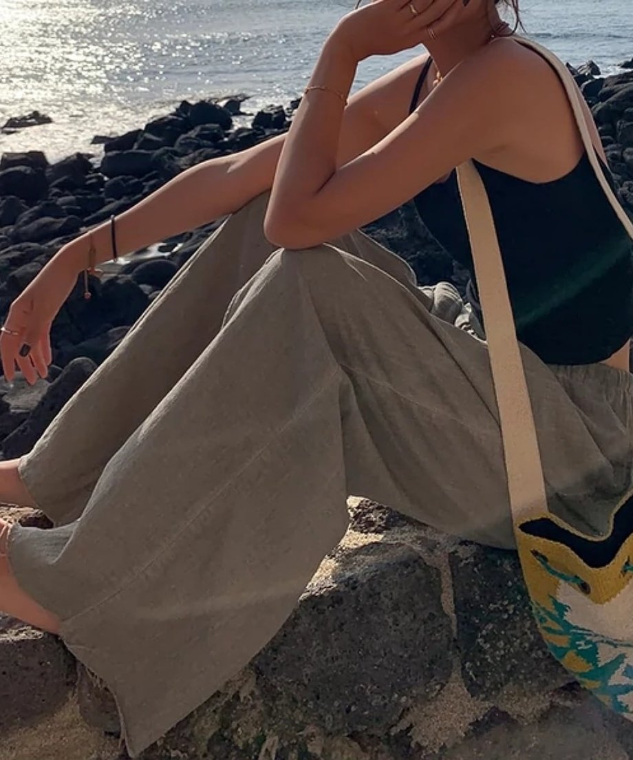岩場に座る女性。ゆったりとしたワイドパンツのボリューム感と海辺のロケーション。
