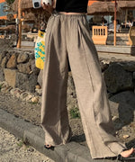 リネン混のカーキグレー色のワイドパンツを履き、黒のキャミソールを合わせた女性の屋外での立ち姿