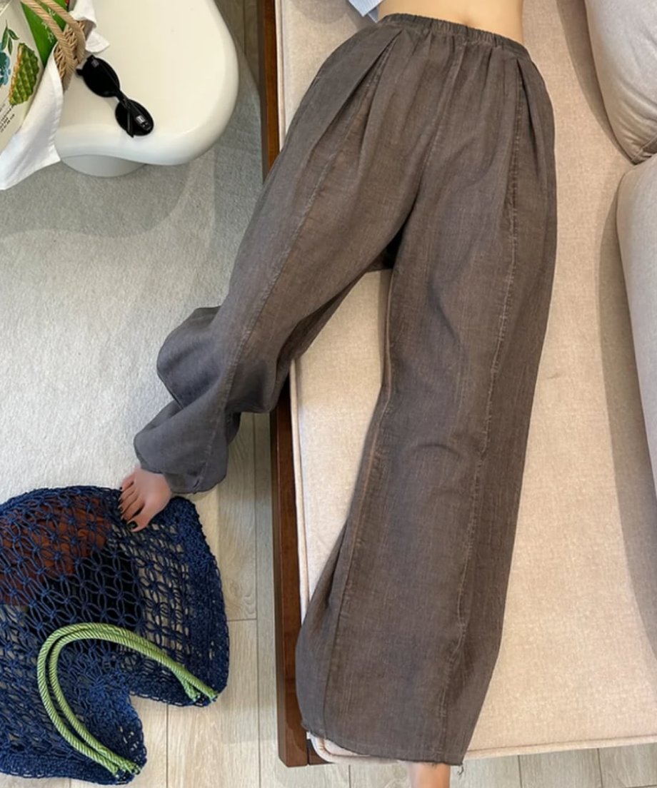 ライトブラウンのワイドパンツをはいた女性がベッドで横になっている写真。足元にはブルーのメッシュバッグが置かれている。
