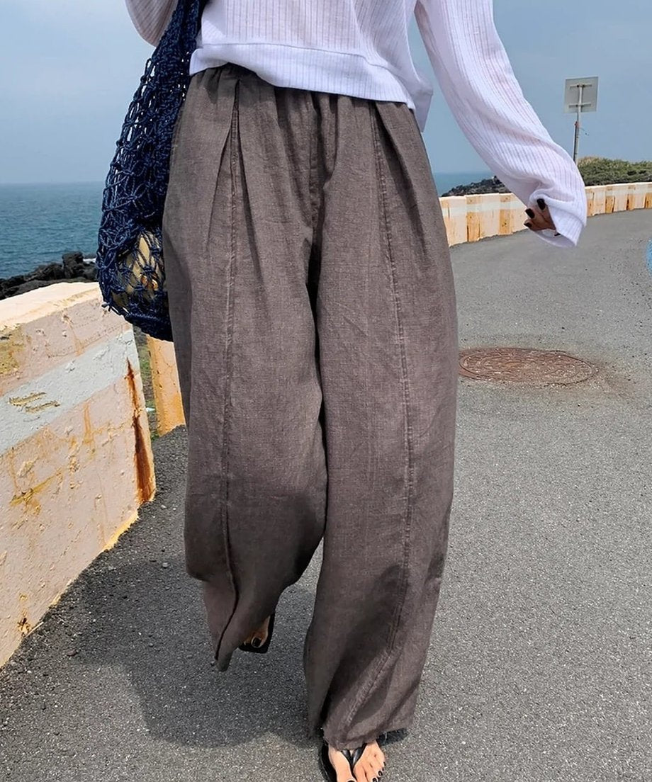 屋外でワイドパンツを着用した女性が海沿いの道を歩いているショット。