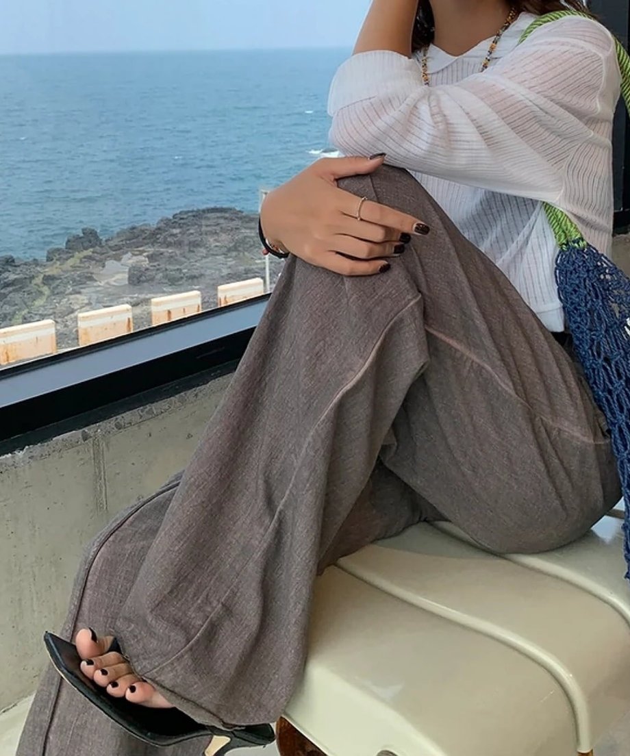 椅子に座る女性。ゆったりとしたワイドパンツのボリューム感と海辺のロケーション。
