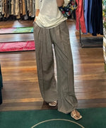 リネン混のカーキベージュ色のワイドパンツを履き店内にいる様子の女性の立ち姿。