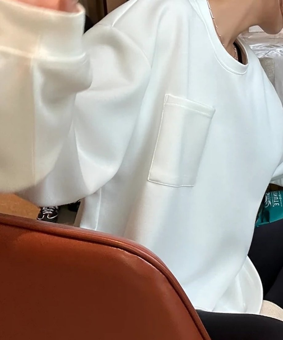 胸元のポケットが特徴的な白いラウンドネックスウェットを着た女性の斜めからのショット。