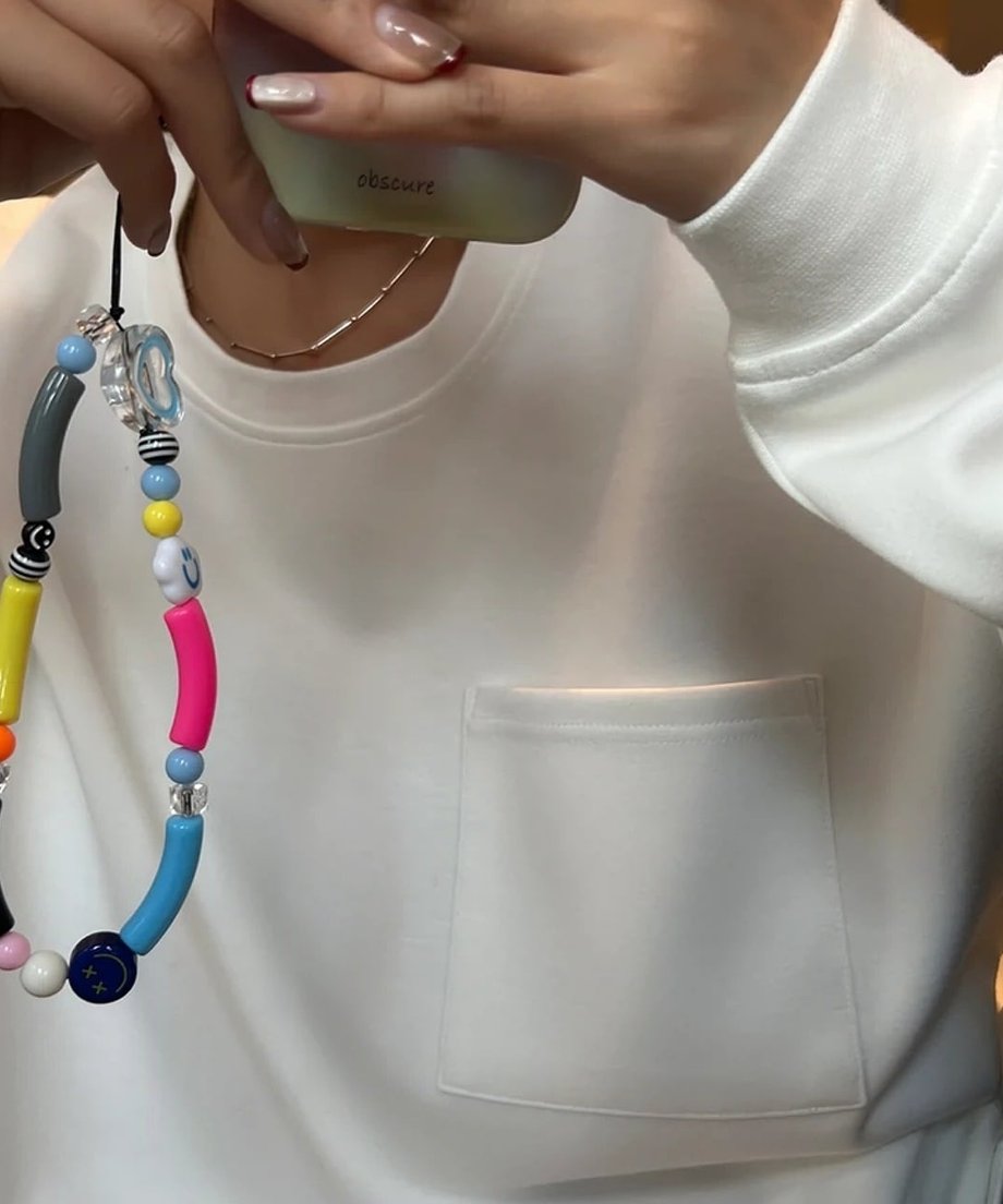 白いプルオーバーの袖口を少し捲り上げ、スマートフォンを操作する女性のアップ