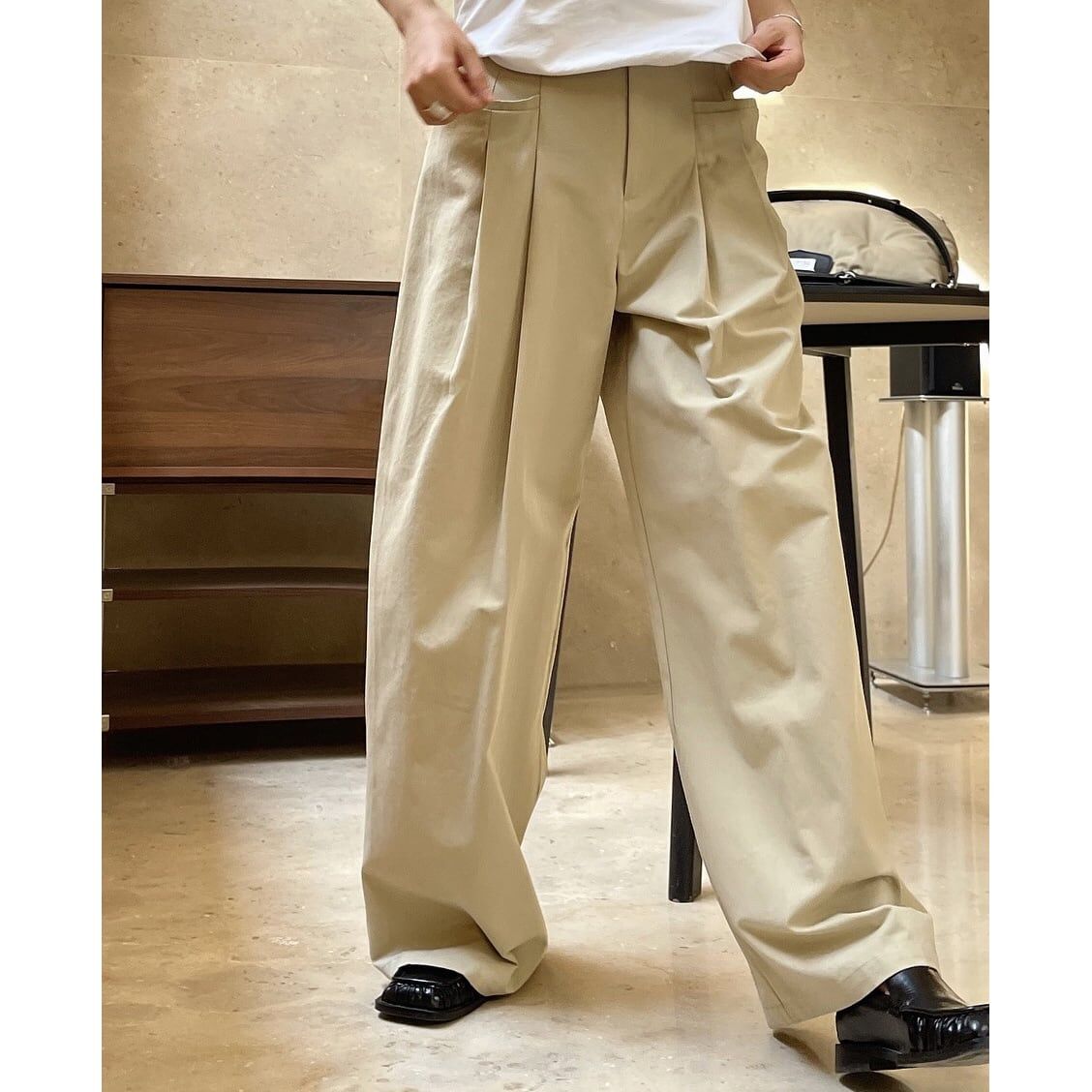 ベージュのワイドパンツを着用した女性の正面クローズアップ。パンツの質感とタックのディテールが確認できる。