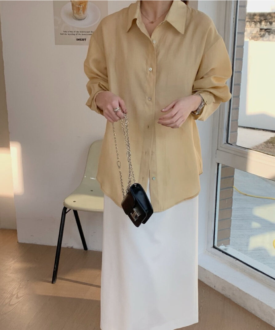イエローのシアー素材の長袖シャツを着用し、黒のミニショルダーバッグを持った女性のショット。