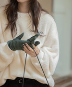 オフホワイトのふわふわしたボア素材のプルオーバーを着た女性のクローズアップ。手袋をした女性がバッグを持っている。