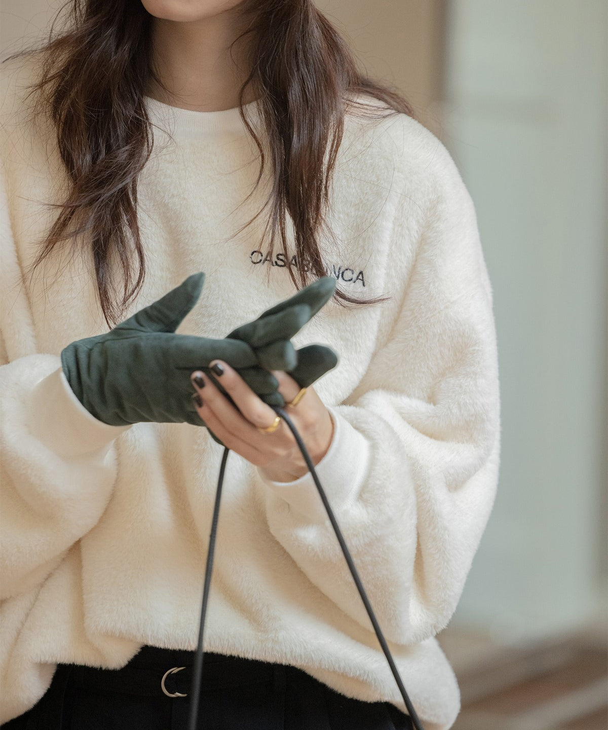 オフホワイトのふわふわしたボア素材のプルオーバーを着た女性のクローズアップ。手袋をした女性がバッグを持っている。