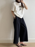 黒色のワイドパンツを履いた人がプリントTシャツとスカーフ、サンダルを着用している。