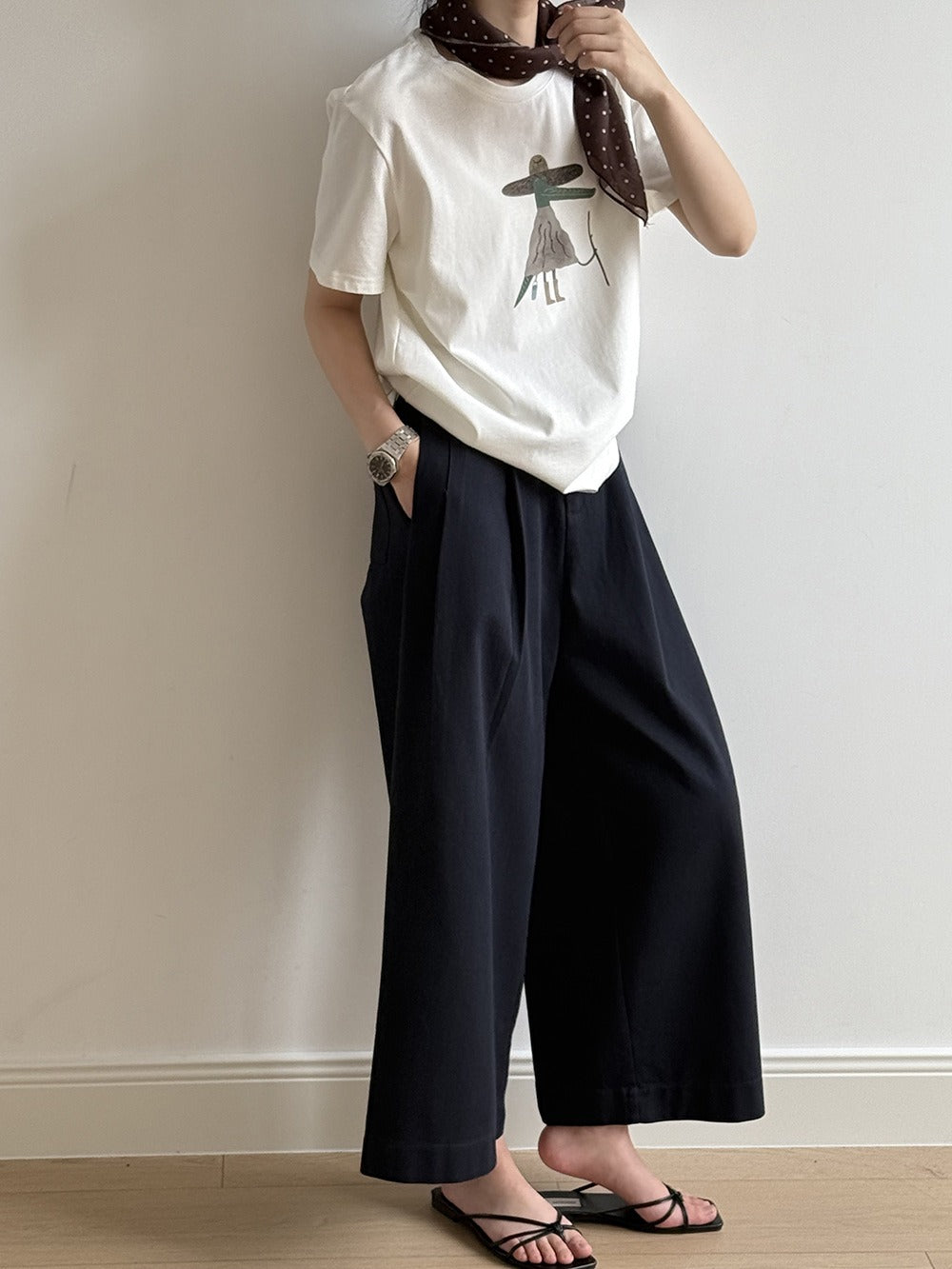 黒色のワイドパンツを履いた人がプリントTシャツとスカーフ、サンダルを着用している。