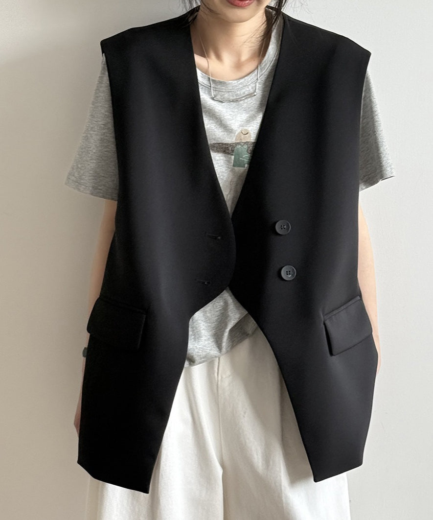黒のオーバーサイズテーラードジレに、グレーのプリントTシャツと白のワイドパンツを合わせた女性の正面。ジレは深めのVネックで、ダブルボタン風のデザイン。