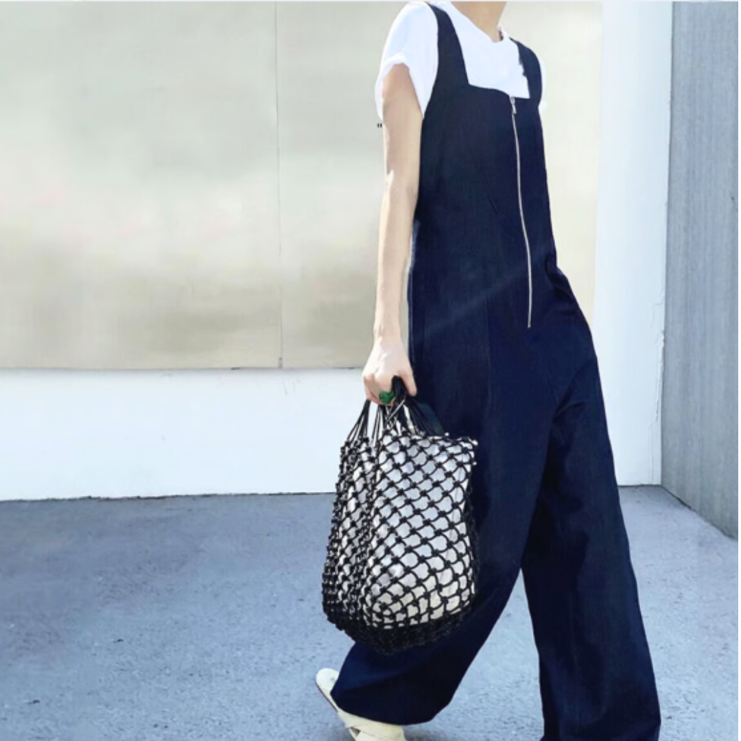 白Tシャツの上にデニムオールインワンを重ね着し、網バッグを持って歩いている女性のクローズアップ写真。