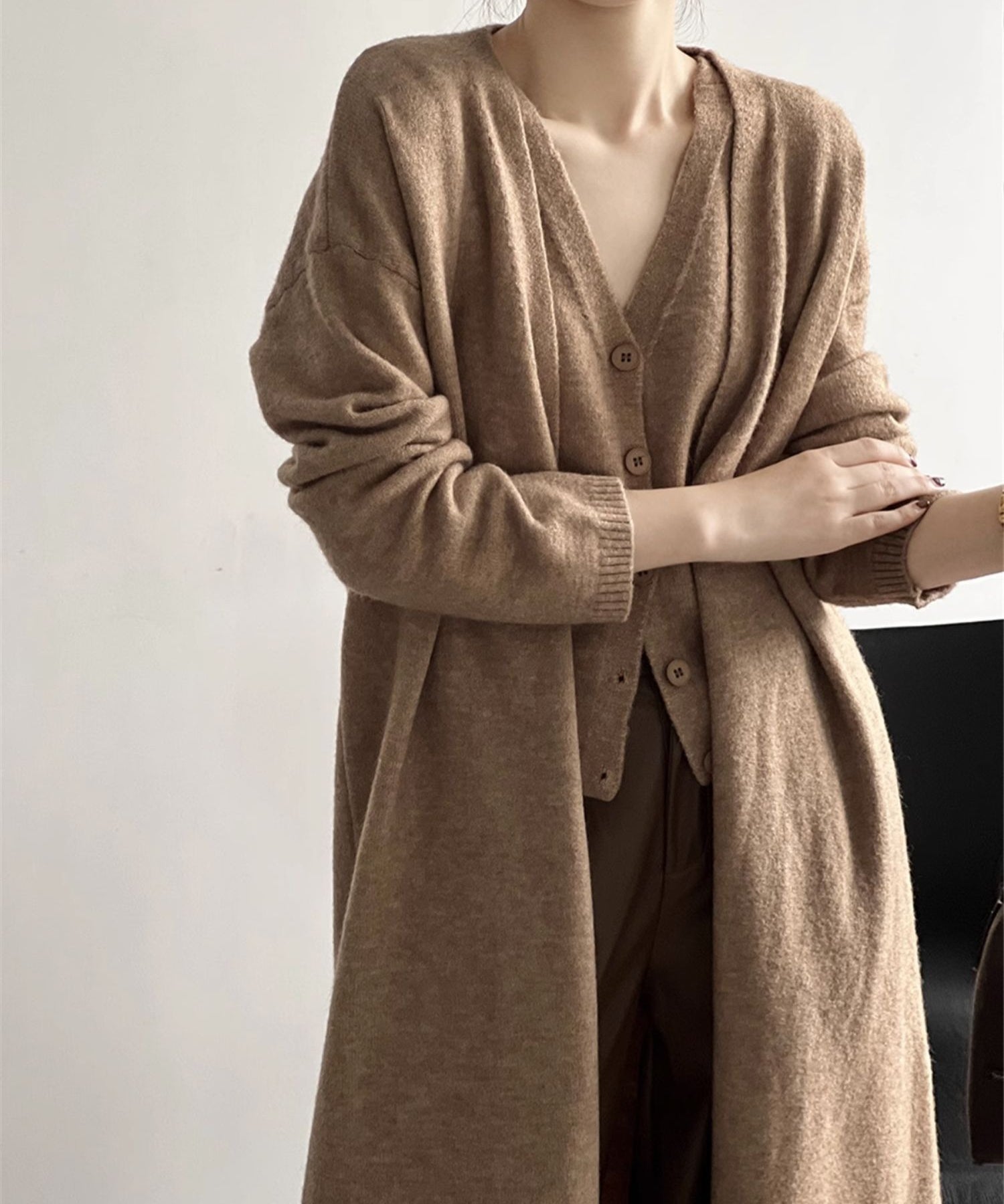 キャメルのロングカーディガンとベストを重ね着し、茶系のワイドパンツと合わせたシックな装いの女性。
