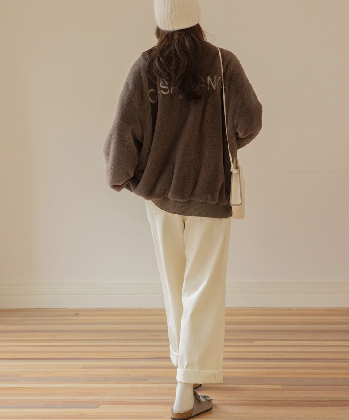 ブラウン色のボアプルオーバーと白のワイドパンツを合わせた、後姿の女性の全身コーディネート。プルオーバーの背中には「CASABLANCA」の白い刺繍ロゴがある。