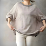 グレージュのプルオーバーを広げるように持った女性、ゆったり感のあるシルエットが際立つ
