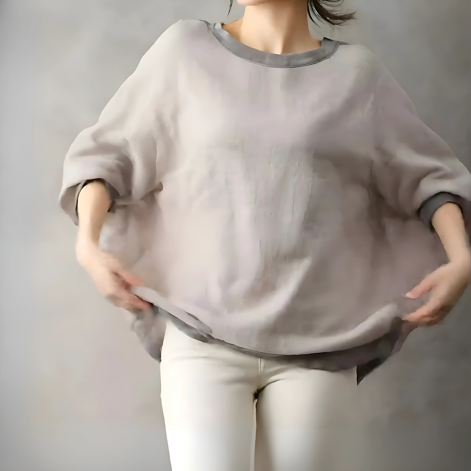 グレージュのプルオーバーを広げるように持った女性、ゆったり感のあるシルエットが際立つ